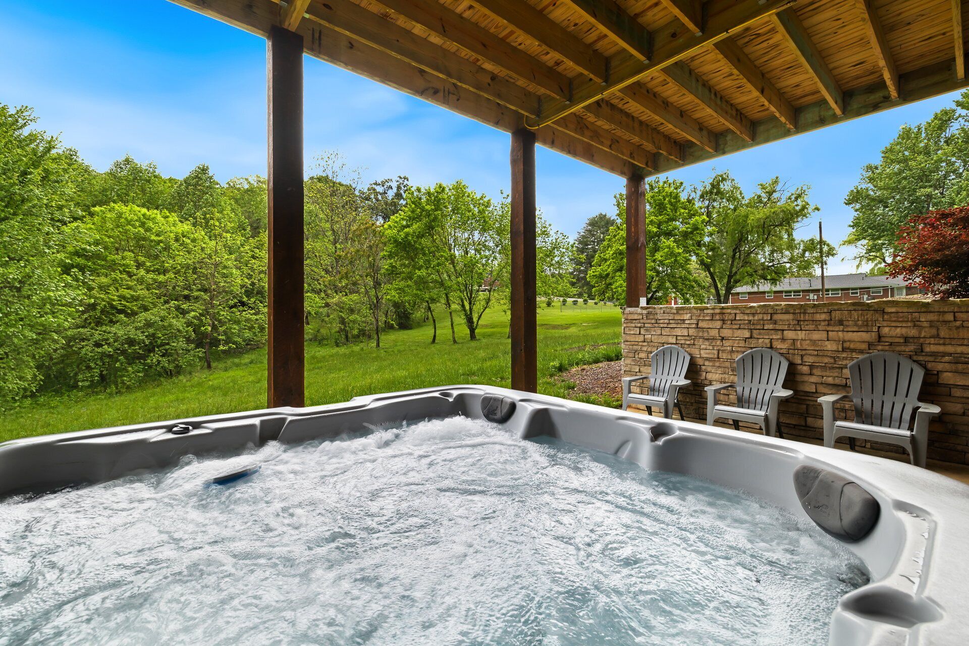 Ein Whirlpool unter einer hölzernen Pergola mit einer Steinmauer und Adirondack-Stühlen.