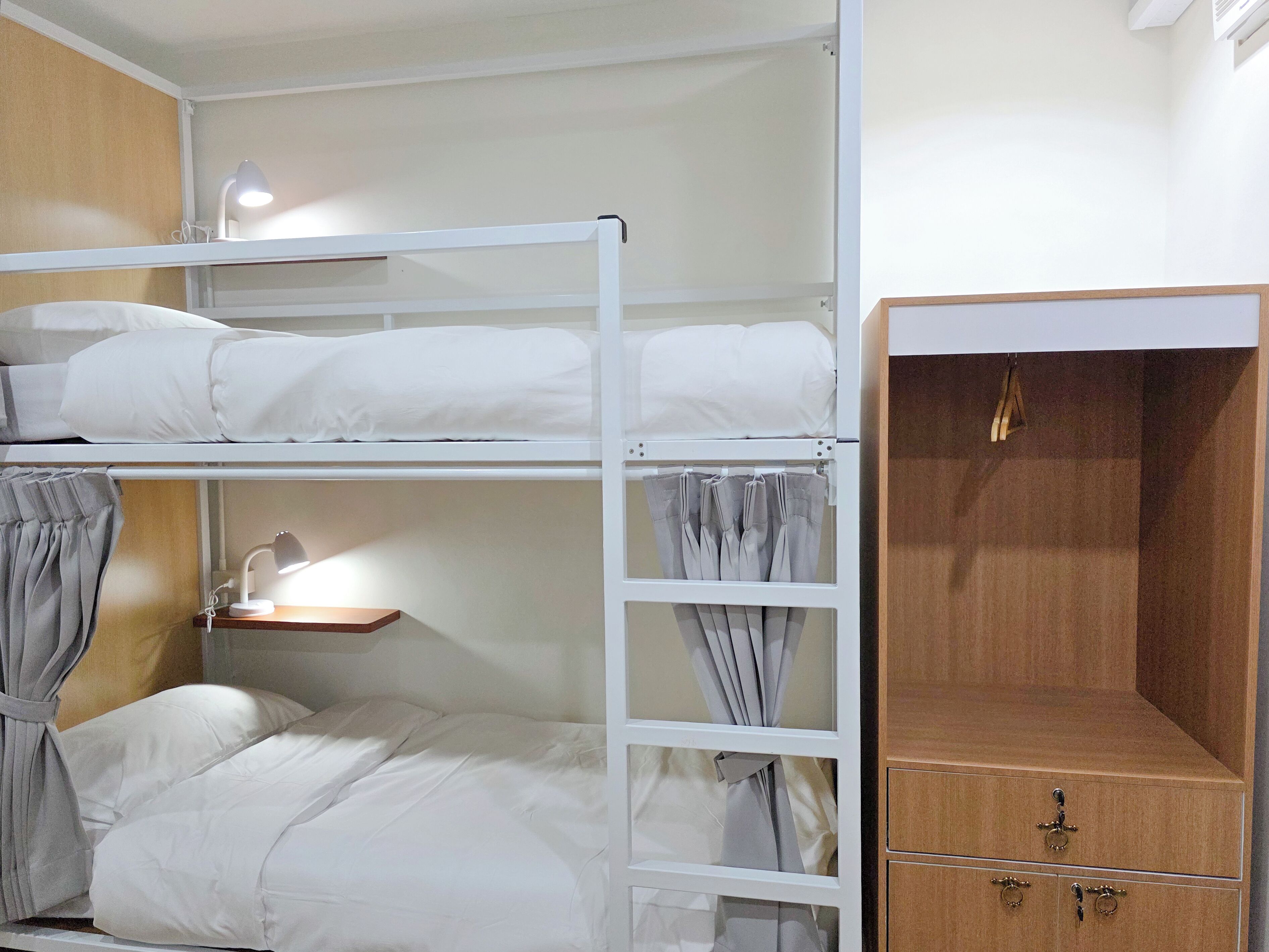 A bunk bed room with a desk and a wooden wardrobe.