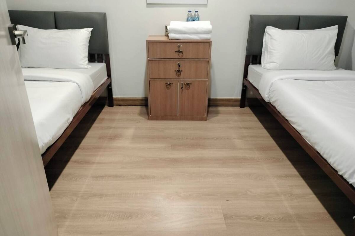 A hotel room with two beds, a wooden dresser, and a small table with water bottles.