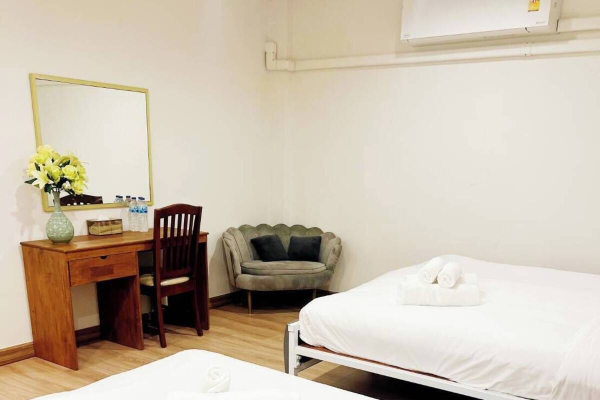 A hotel room with two single beds, a wooden desk with a mirror, a chair, and a sofa.
