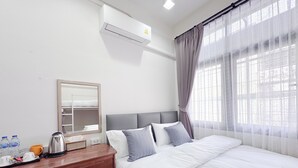 Habitación de hotel con una cama, un escritorio con hervidor, un espejo y aire acondicionado.