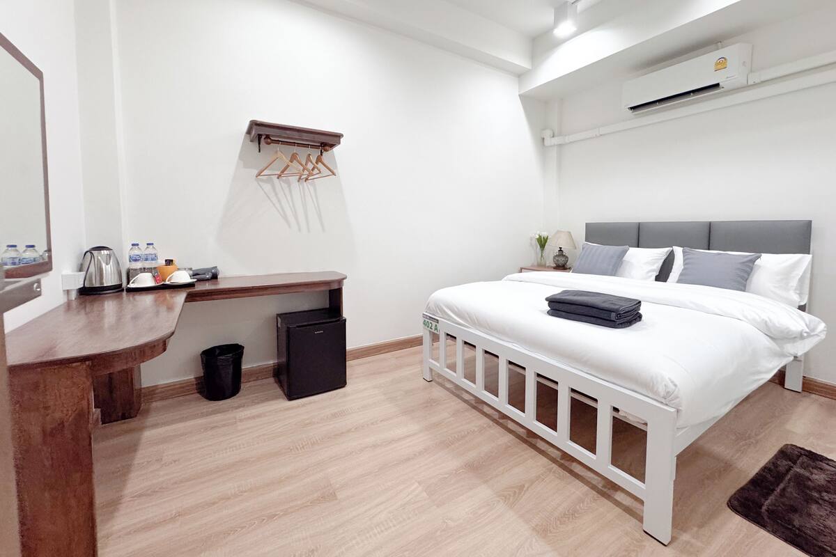 A modern bedroom with a white bed, grey headboard, and a wooden desk with a mirror.