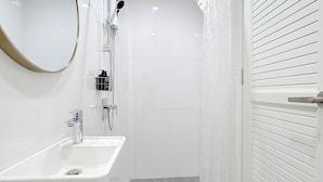 Un baño moderno con un lavabo blanco, una ducha con puerta de vidrio y un espejo con marco dorado.