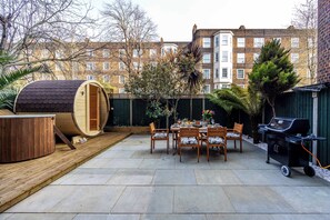 Une terrasse avec un jacuzzi, une plateforme en bois, un barbecue et une table à manger avec des chaises.