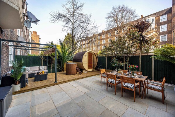 Une terrasse avec une table et des chaises en bois, un tonneau en bois et un ensemble de canapés.