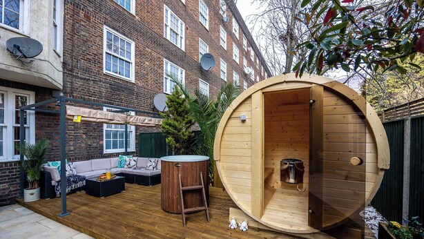 A wooden sauna in a backyard with a sofa and a table. - Modern 4 Bed Flat | Prime Central London Location (Greater London)
