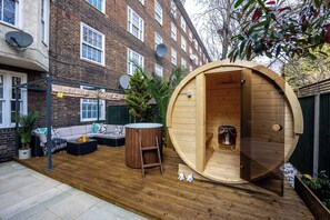 A wooden sauna in a backyard with a sofa and a table.
