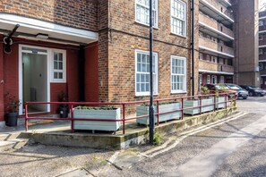 Un bâtiment en briques rouges avec une porte blanche, des fenêtres et une rambarde rouge.