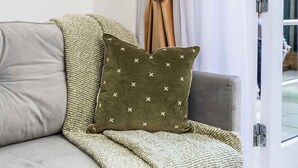 A modern living room with a grey sofa, a green throw blanket, and a patterned pillow. - Modern 4 Bed Flat | Prime Central London Location (Greater London)