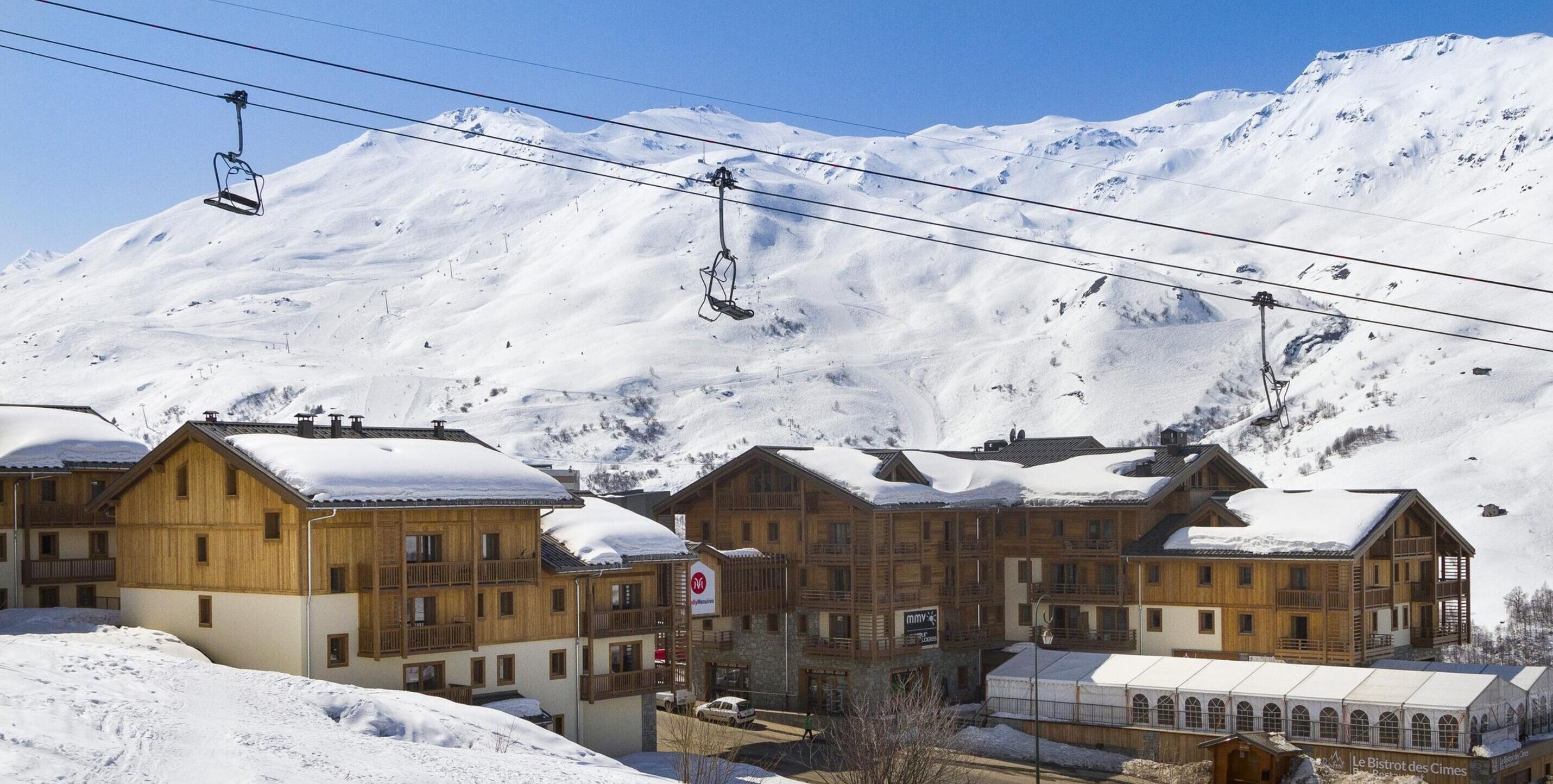 A ski resort with wooden buildings, ski lifts, and a snowy mountain backdrop.