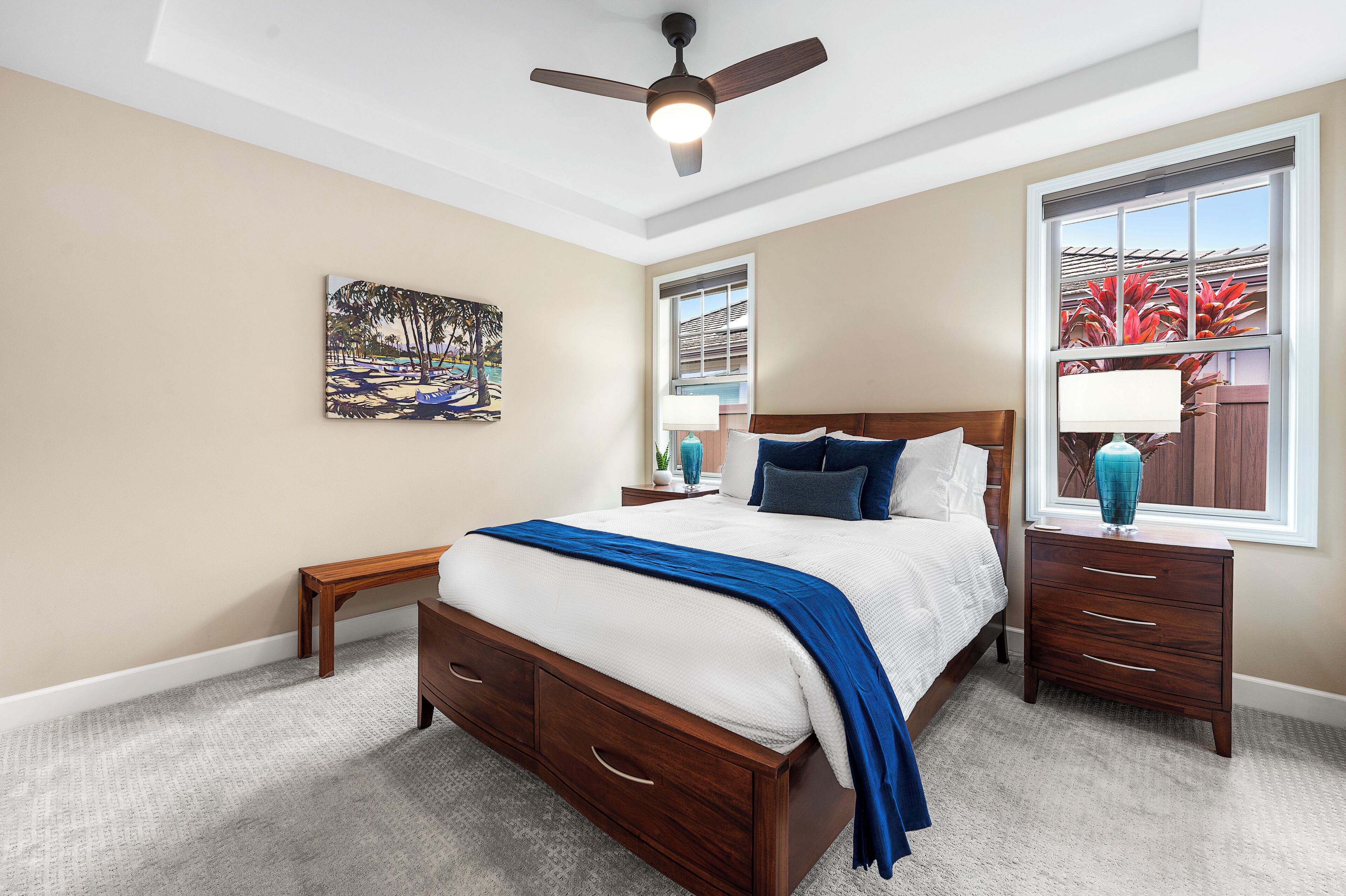 A bedroom with a bed, nightstands, a ceiling fan, a window with a view, and a painting on the wall.