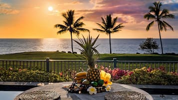 Un décor tropical avec une terrasse en bois, un centre de table décoré d’ananas et une vue sur l’océan au coucher du soleil.