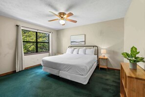 Une chambre à coucher avec un lit, un ventilateur de plafond, une fenêtre avec des rideaux, une table de chevet avec une lampe et une plante.