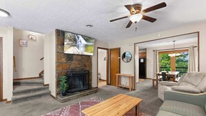 A living room with a stone fireplace, a ceiling fan, a sofa, and a dining area visible through an open door. - Near Dollywood・Pet Friendly・Sleeps 8・Pool・Grill (Pigeon Forge)