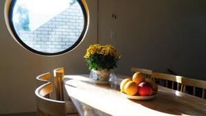 Un coin repas avec une table ronde, des chaises, une plante en pot et un saladier de fruits.