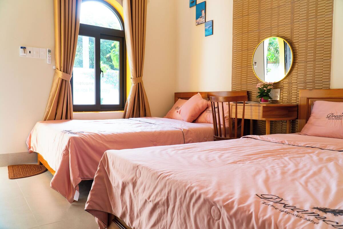 A bedroom with two beds, a wooden desk, a mirror, and a window with curtains.