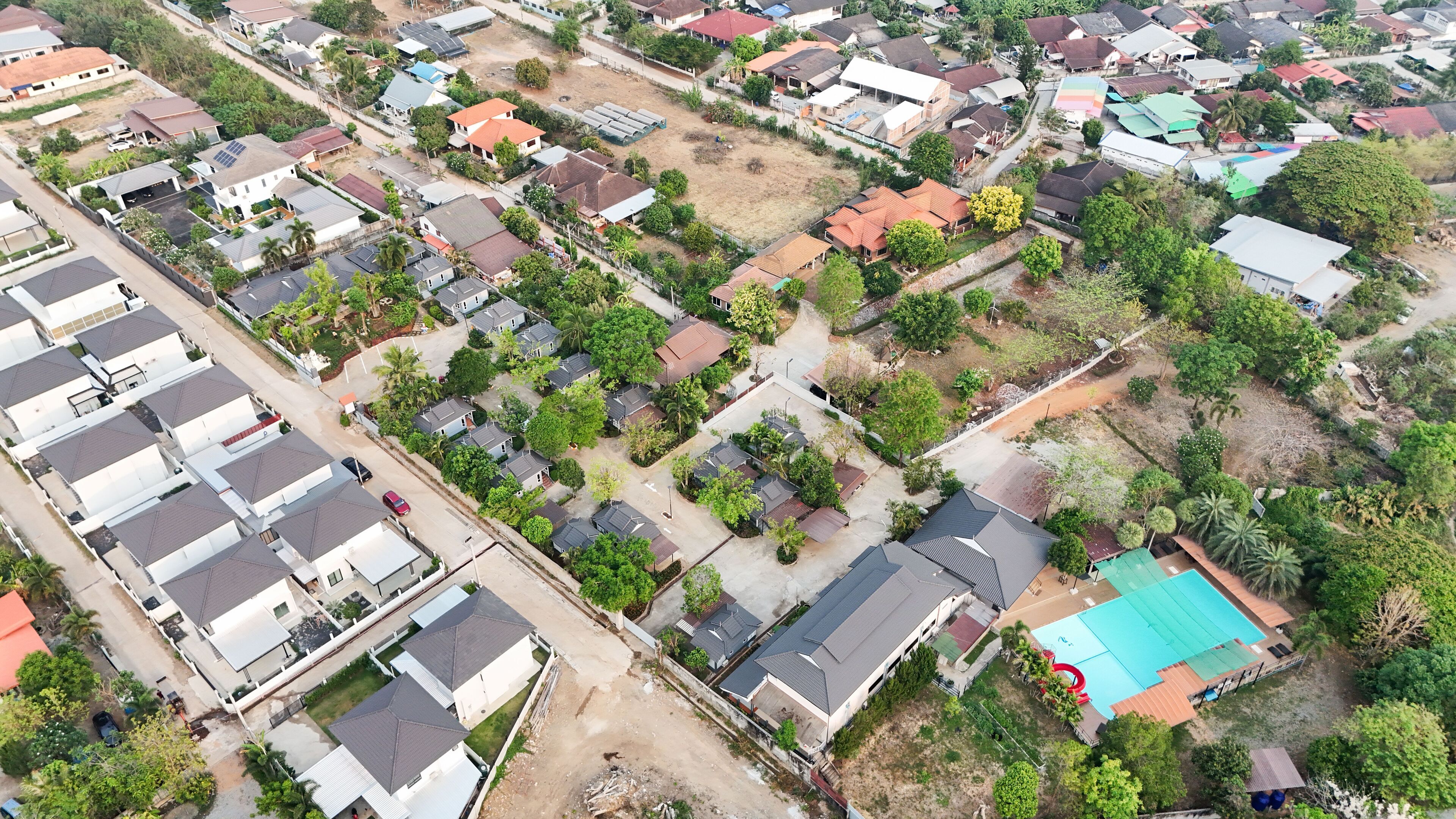 Luchtbeeld van een woongebied met meerdere huizen, waarvan sommigen zonnepanelen hebben, omgeven door groen en enkele open ruimtes.