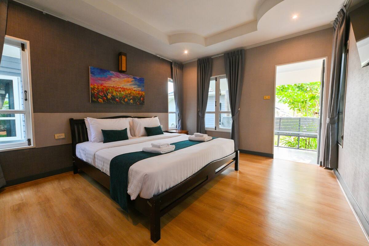 A hotel room with a large bed, a painting on the wall, and a view of the outdoors.