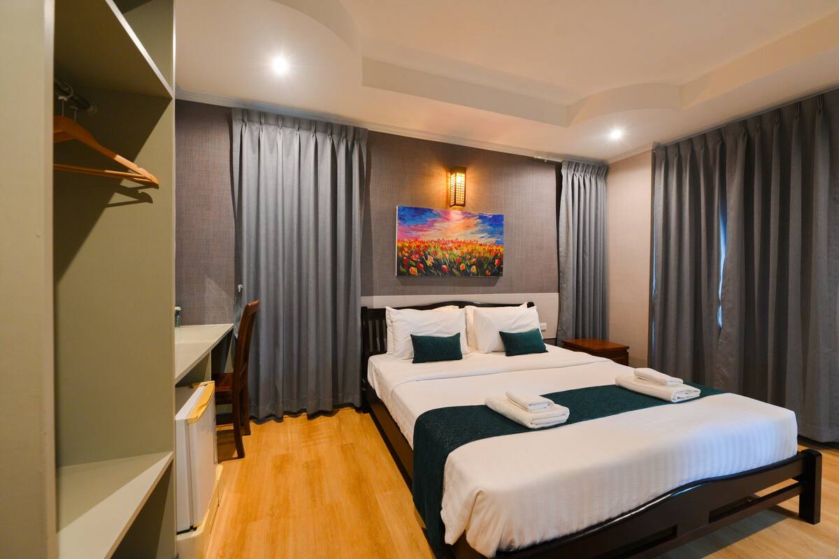 A hotel room with a bed, a desk, a chair, a painting, and curtains.