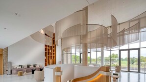A modern interior with a curved reception desk, a seating area with sofas, and a large window offering a view of the outdoors. - Apartment in Baillargues Near Golf Course (Baillargues)