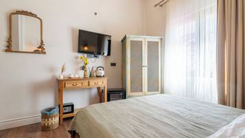 A bedroom with a bed, a TV mounted on the wall, a wardrobe, a desk with a mirror, and a window with curtains.