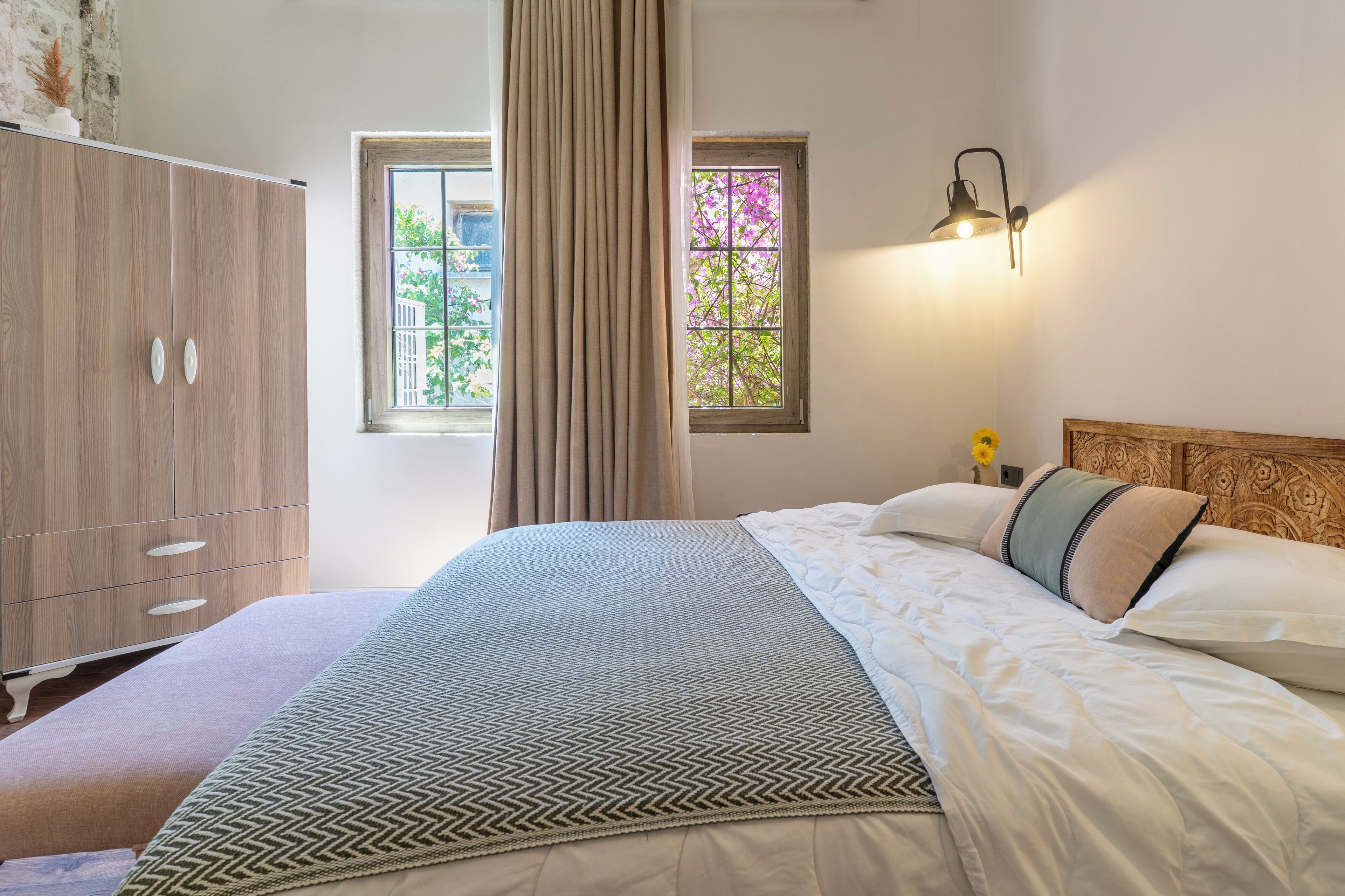 A bedroom with a bed, a wardrobe, a window with curtains, and a wall-mounted lamp.
