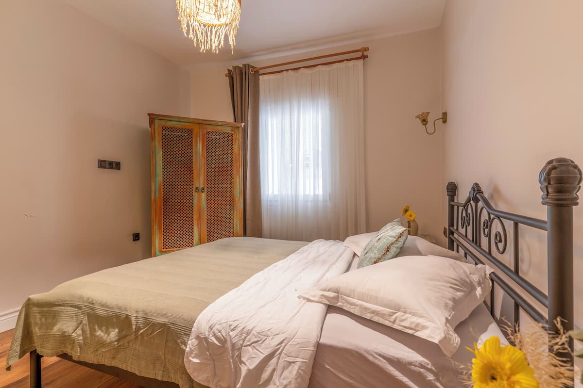 Un dormitorio con cama, armario, ventana con cortinas y una lámpara de pared.