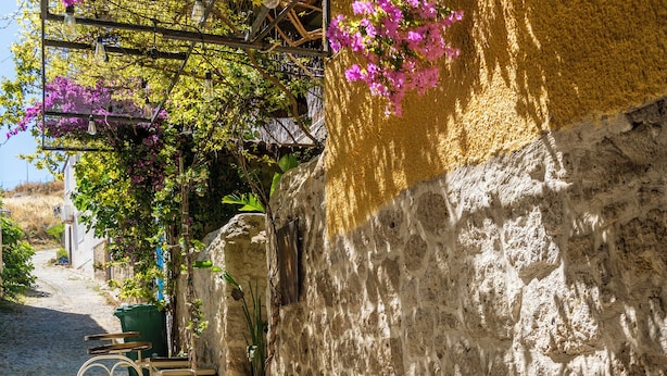 A cobblestone street with outdoor seating, including tables and chairs, and a stone wall with a climbing plant. - Mediha Hanım Konağı Alaçatı (Cesme)