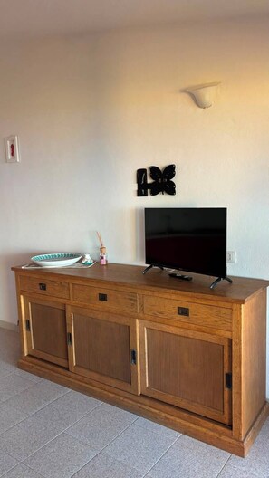 A wooden TV stand with a flat-screen TV, a decorative butterfly, and a small framed picture on the wall. - Charming apartment with sea view in Costa Paradiso – Terrace, relax and nature (Costa Paradiso)