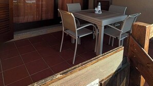 A room with a dining table and chairs, a window with curtains, and a wooden fence. - Charming apartment with sea view in Costa Paradiso – Terrace, relax and nature (Costa Paradiso)
