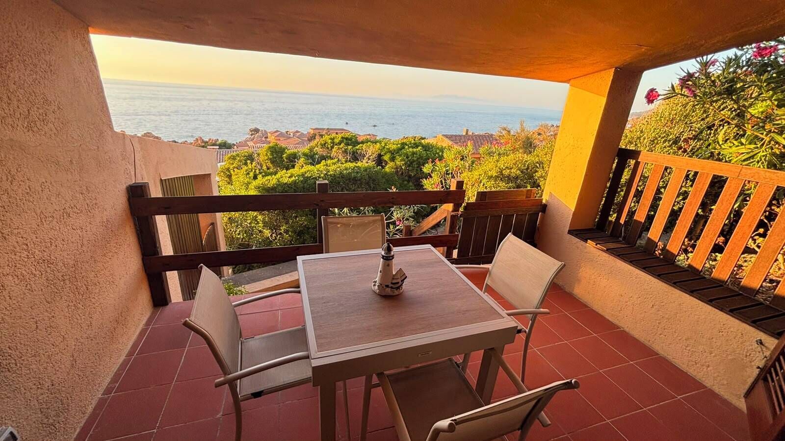 A balcony with a table and chairs, overlooking a coastal view.