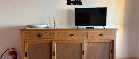Un mueble de madera con un televisor de pantalla plana encima, un extintor a la izquierda y un adorno con forma de mariposa colgado en la pared.