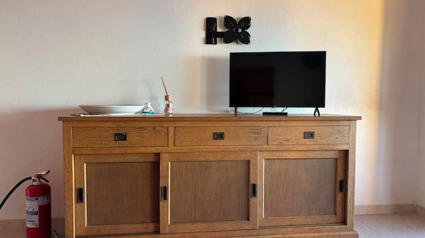 Un mueble de madera con un televisor de pantalla plana encima, un extintor a la izquierda y un adorno con forma de mariposa colgado en la pared.