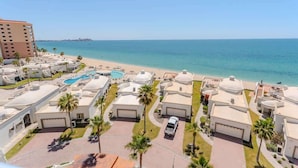 Een resort met meerdere gebouwen met witte daken, een zwembad en uitzicht op het strand.