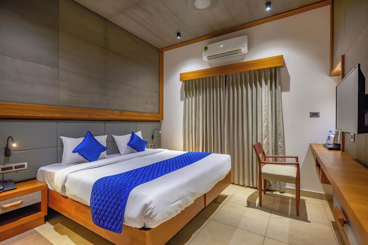 Une chambre d’hôtel avec un grand lit, un bureau, une chaise, un appareil de climatisation et un téléviseur.