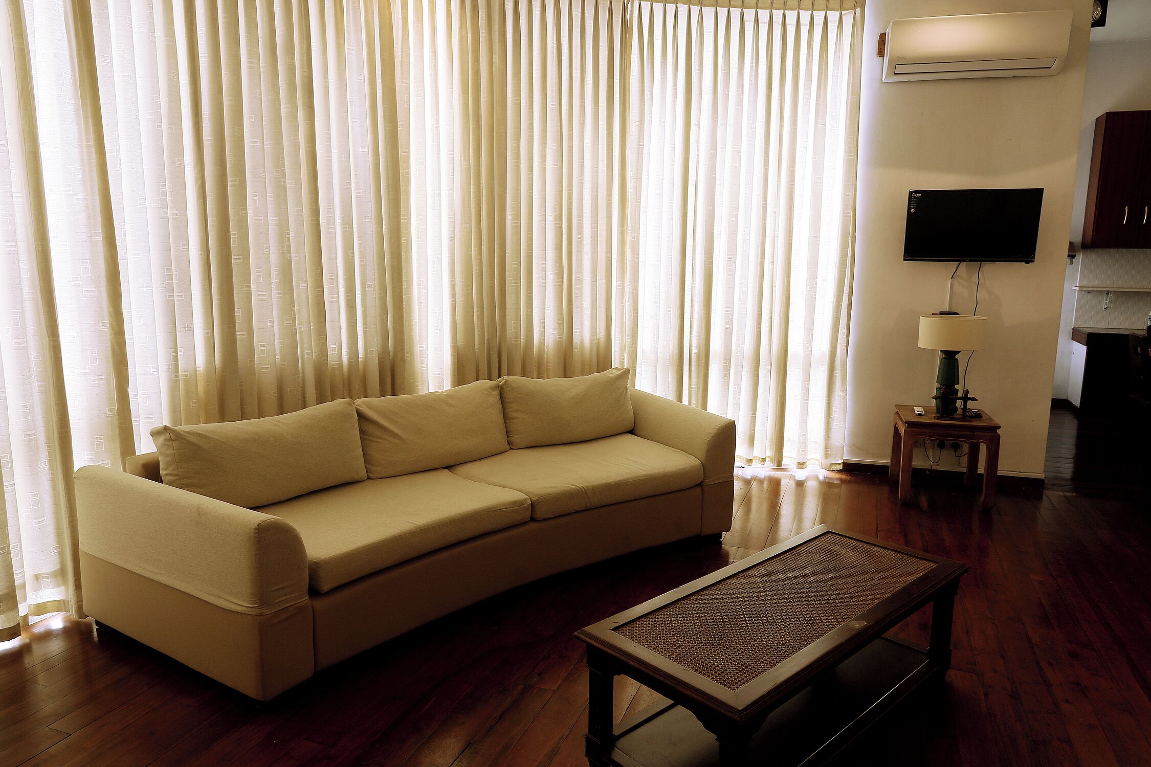 A living room with a beige sofa, a wooden coffee table, and a TV mounted on the wall.