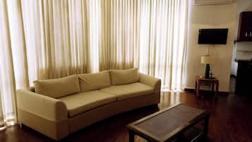 A living room with a beige sofa, a wooden coffee table, and a TV mounted on the wall.