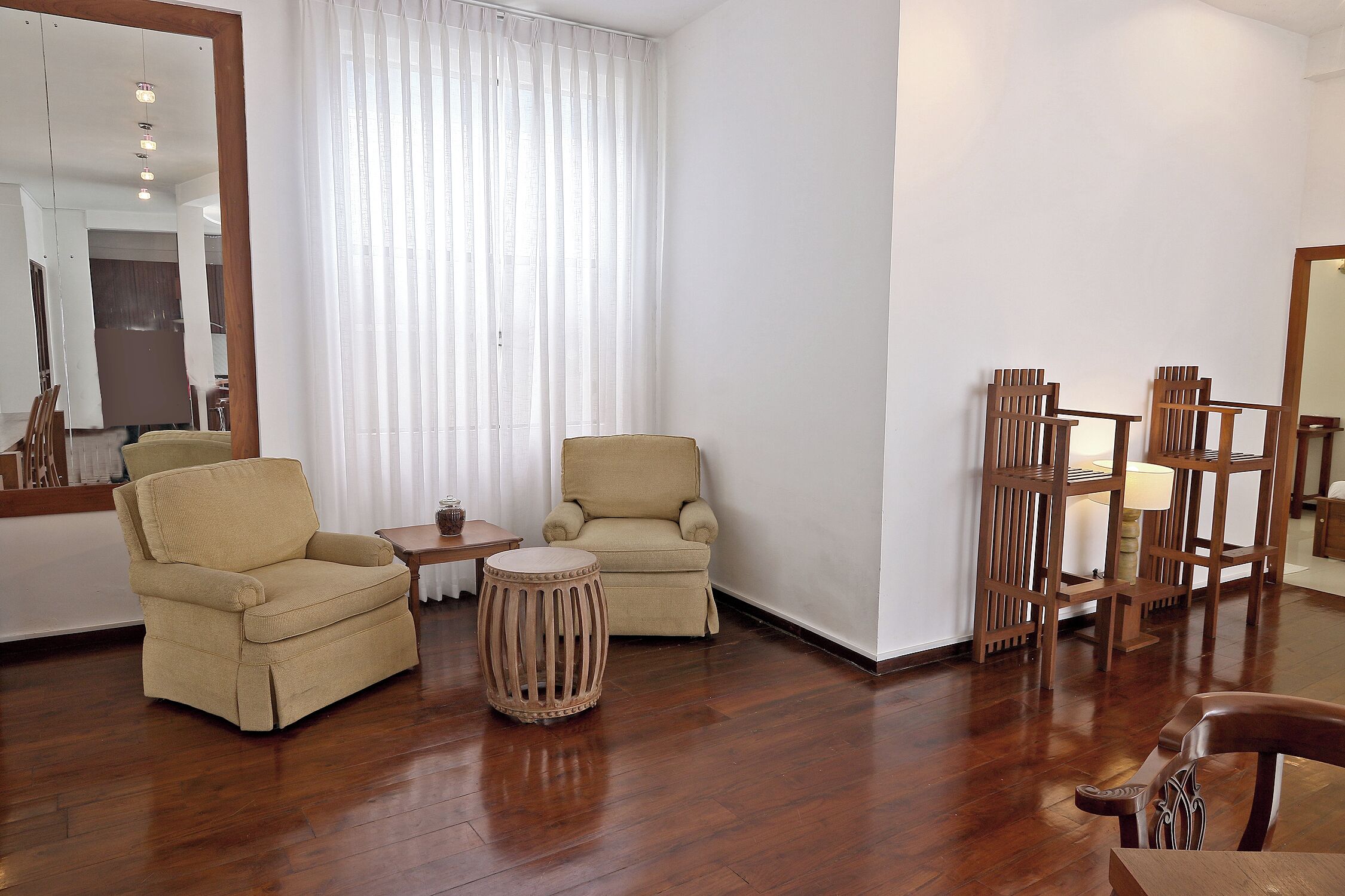 Una habitación con piso de madera, dos sillones color beige, una mesita redonda y una mesita auxiliar de madera.