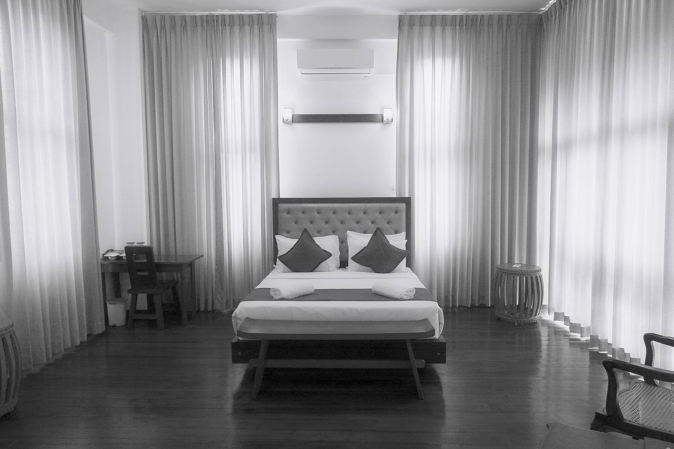 Un dormitorio moderno con una cama grande, una mesita de noche, una silla y un taburete pequeño.