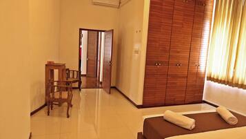 A hotel room with a bed, a wooden wardrobe, a small table with chairs, and a door leading to another room.