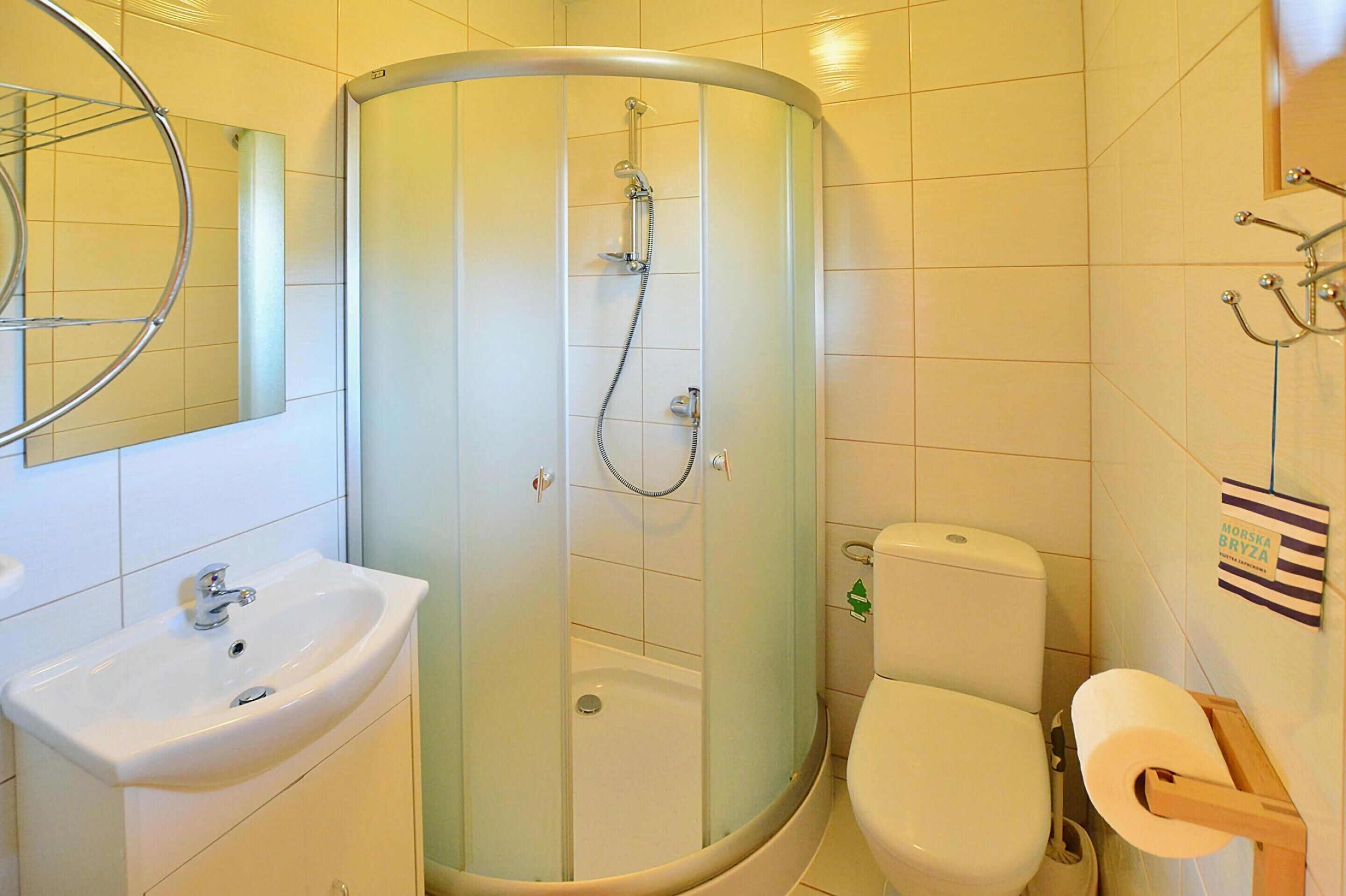 Un baño con ducha envuelta en vidrio, un lavamanos, un inodoro y un espejo.
