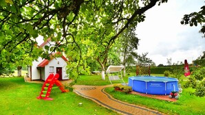 A garden with a red slide, a white building with a red roof, and a blue pool. - Large Holiday Home With a Beautiful Garden (Slawno)