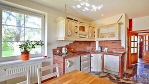 A kitchen with a wooden table, white chairs, a potted plant, and a brick backsplash. - Large Holiday Home With a Beautiful Garden (Slawno)
