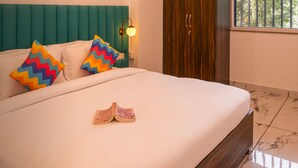 Una cama bien hecha con ropa blanca y almohadas de diseño zigzag en colores vivos, un cabecero color turquesa y una lámpara de noche.