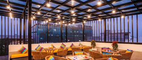 Una terraza con iluminación atractiva y vistas a la ciudad, con mobiliario de mimbre y techo de cristal.