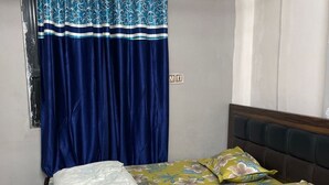 A bed with floral bedding, a blue curtain, and a wooden headboard. - Hotel yes (Jaipur)