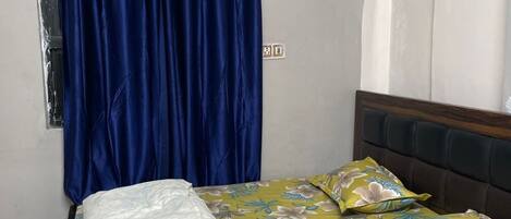 Ein Bett mit Blumenmuster auf der Bettwäsche, einem blauen Vorhang und einem hölzernen Kopfteil.