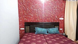 A room with a red patterned bedspread, a dark headboard, and two patterned pillows. - Hotel yes (Jaipur)
