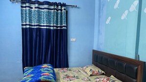 A bedroom with a bed, a blue curtain, and a floral bedspread. - Hotel yes (Jaipur)