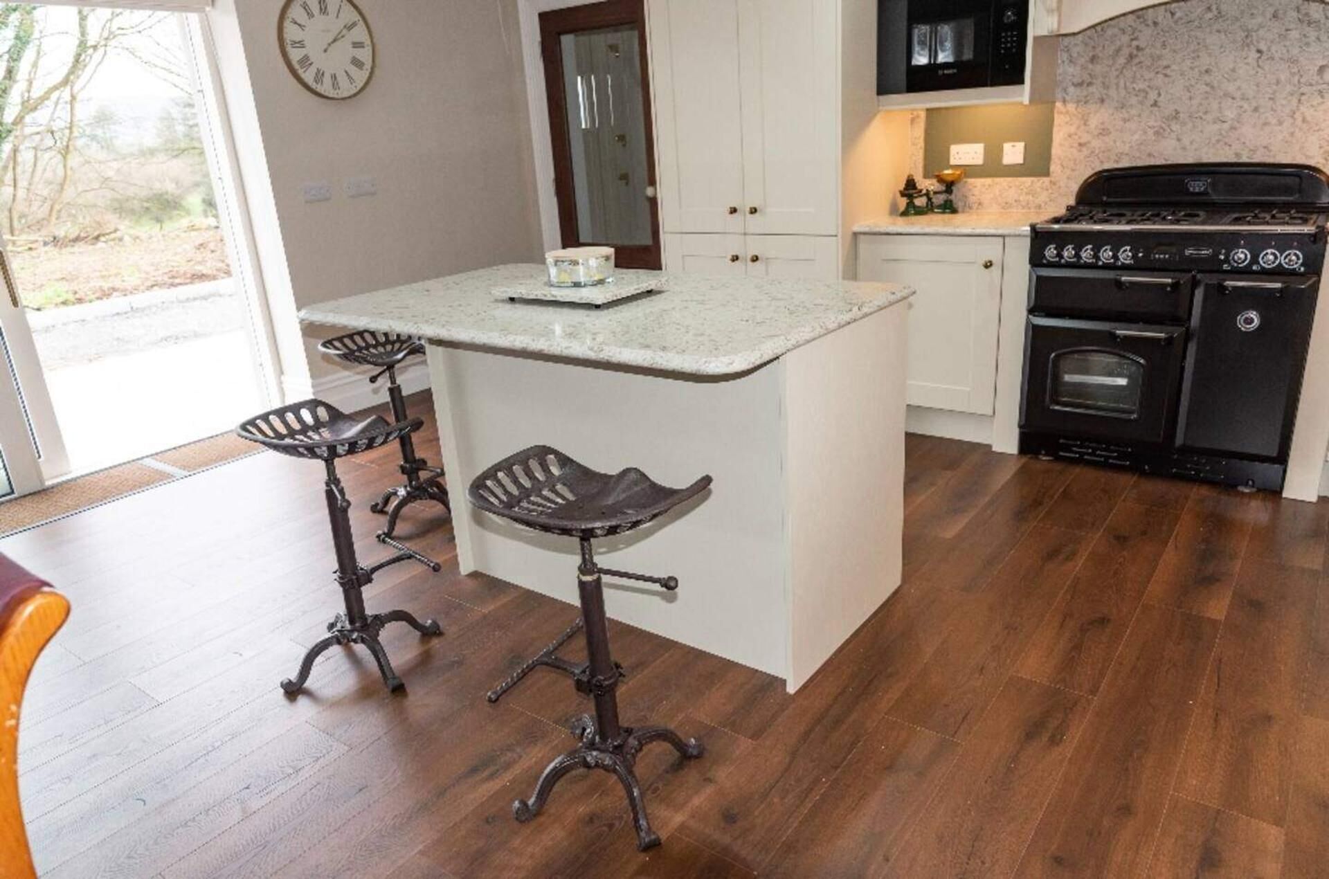 A kitchen with a central island, two bar stools, a stove, and a microwave.